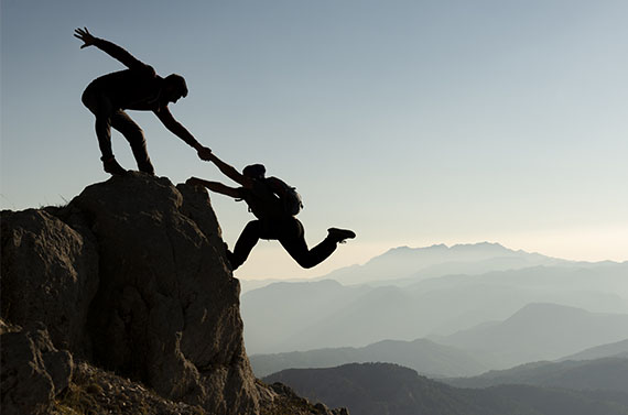 Silhouette of a man helping another man up a mountain